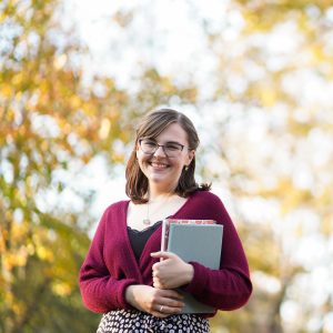 Dorian Bayles smiling outside holding books. Dorian Bayles is a therapist in Alabaster, AL & offers therapy online as well. Learn more here!