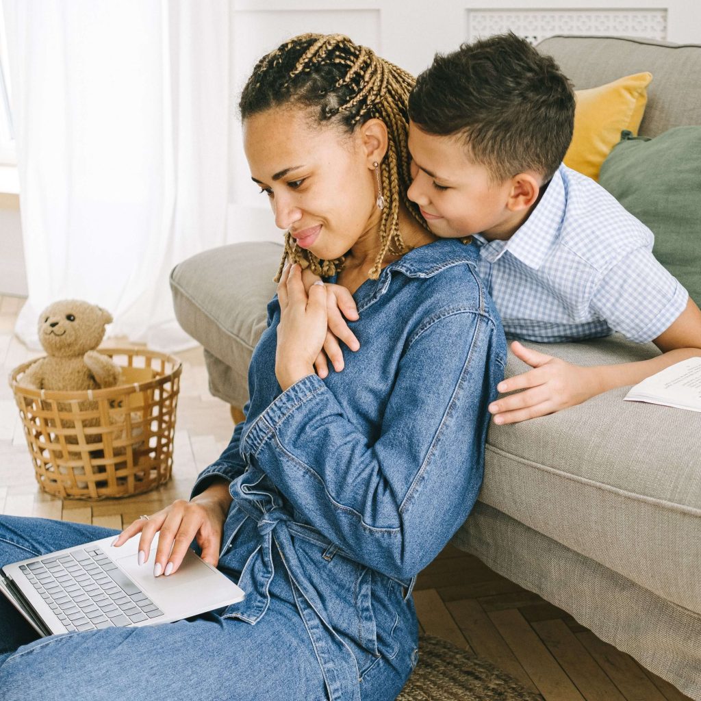 A Black mother & her son gently hugging eachother on the couch while mom searches online. Are you looking for counseling services under BCBS insurance? Explore IHS here!