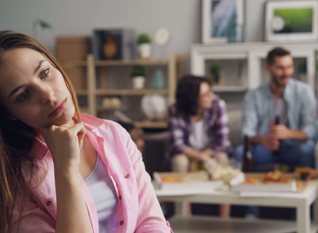 A woman wearing a pink shirt standing away from a group of friends, pondering something. Chronic pain can affect your daily living, especially with sensory overload. Learn how chronic illness therapy in Alabaster, AL can help.